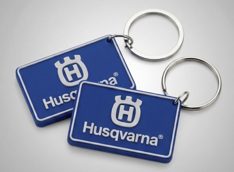 Niebieskie, prostokątne breloki z miękkiego PVC z wypukłym, białym logo Husqvarna. Trwałe breloczki do maszyn i urządzeń.