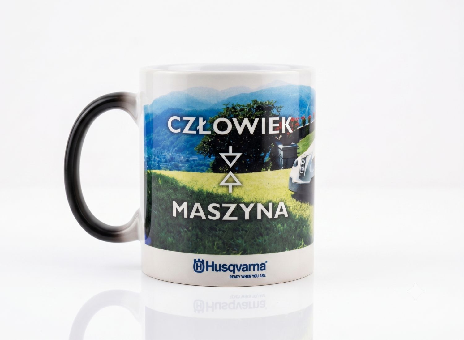 Kubek reklamowy z pełnokolorowym nadrukiem krajobrazu i hasłem człowiek maszyna. Trwała sublimacja z logo dla firm z branży przemysłowej.