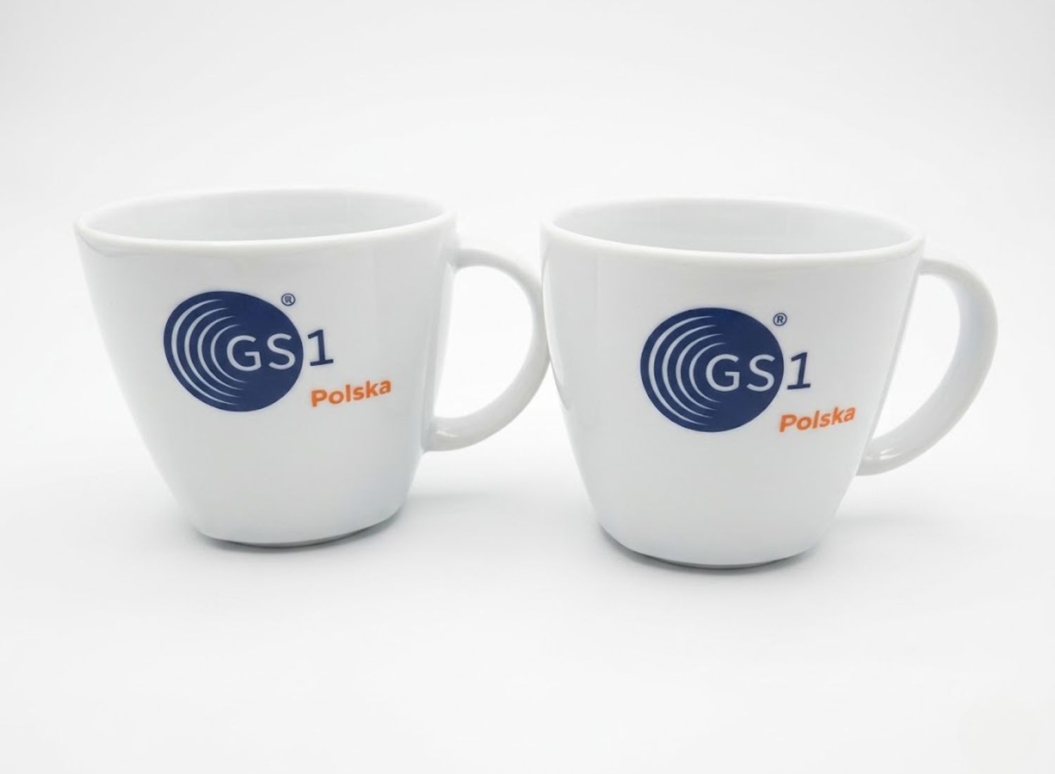 Dwie białe filiżanki biurowe z kolorowym nadrukiem logo GS1 Polska. Klasyczna ceramika reklamowa dla firm.